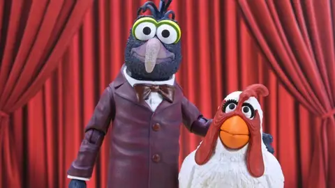Bonecos articulados Gonzo e Camilla da linha Ultimate dos Muppets diante de cortina vermelha de palco